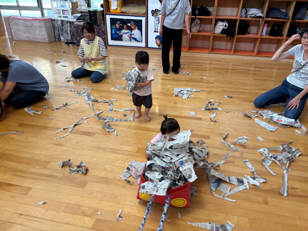 こあらの日の新聞紙遊びで 箱車に新聞紙がいっぱいで乗っている子が見えないくらいになっているところ