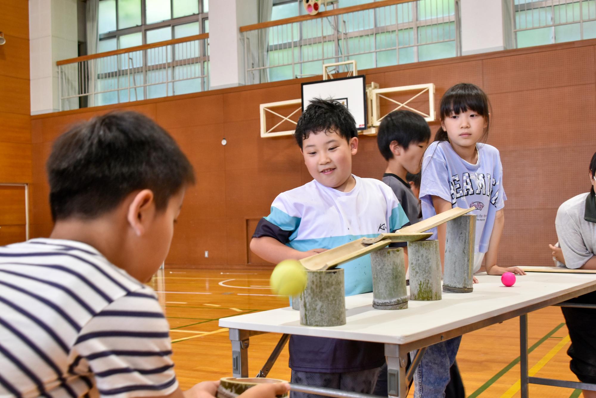 竹で作った装置でボールを転がしキャッチする生徒