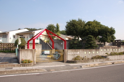 緒川新田保育園の外観を写した写真。手前が道路、正面に門があり、奥に建物がある。