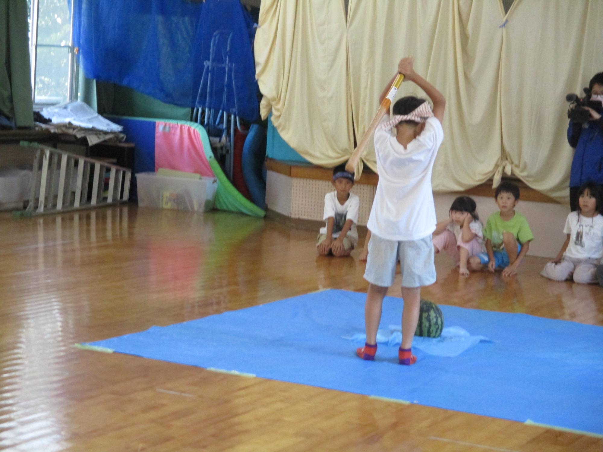 スイカ割りで棒を振り上げる男児