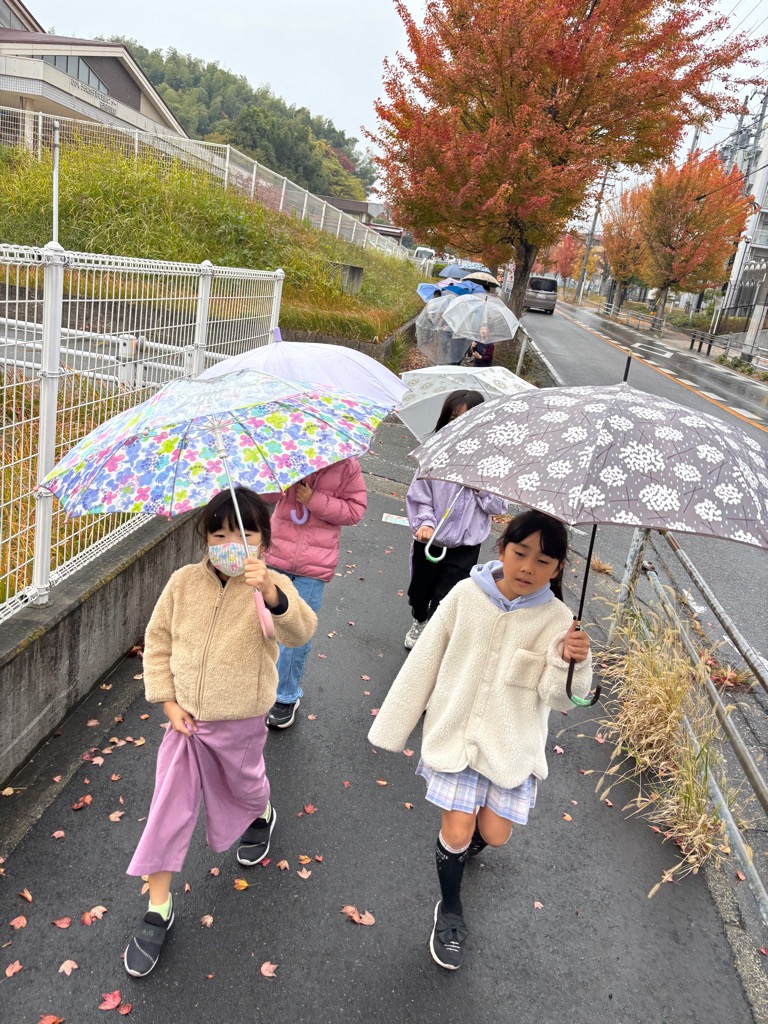 雨の中傘をさして老人ホーム敬愛苑まで出発しているこどもたち
