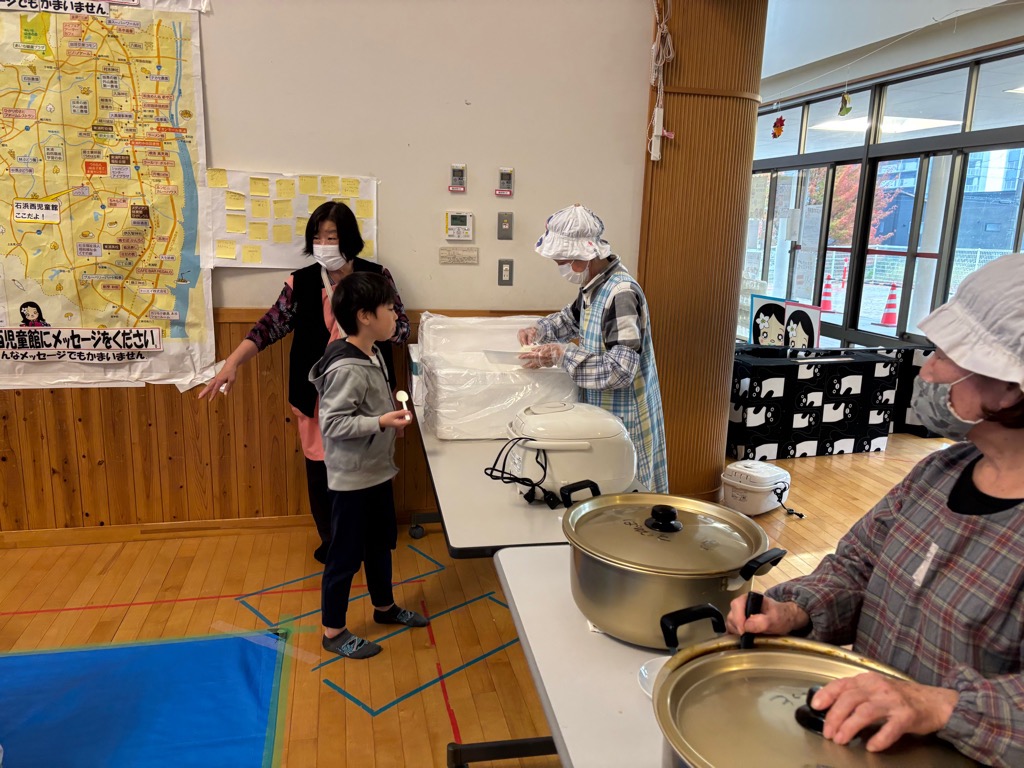 地域食堂パレットさんがカレーをお代わりしに来た子どもにごはんをよそっているところ