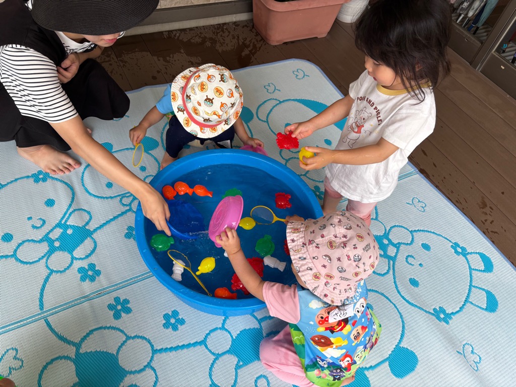 たらいに水を張ったおもちゃの魚で幼児が魚すくいをしているところ