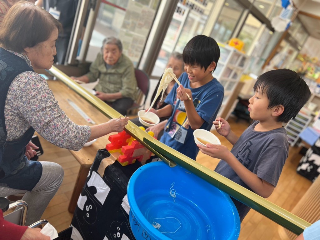 敬愛苑のおばあちゃんと会話をしながら嬉しそうに流れてきたそうめんをつかんでいる男の子たち