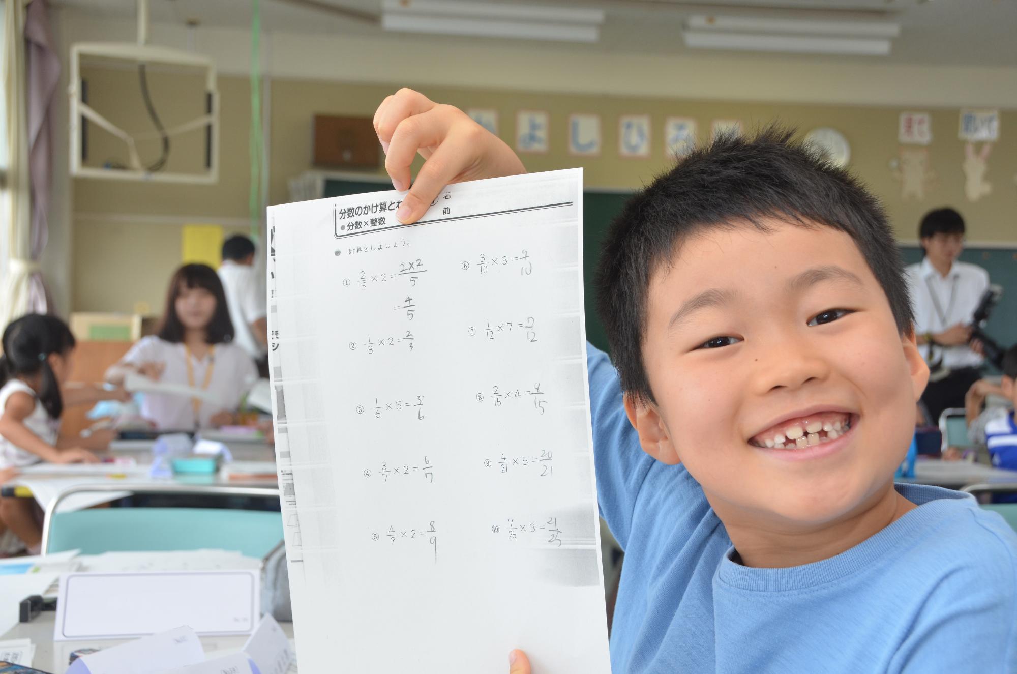 解き終わった課題プリントを笑顔で見せる小学生