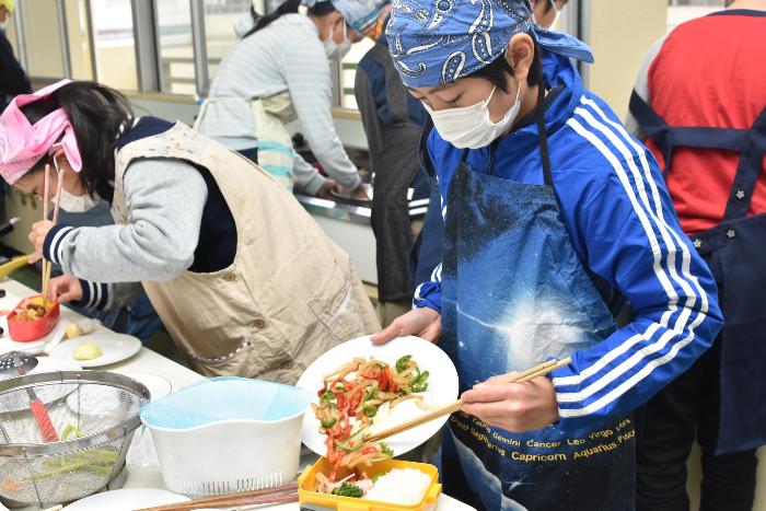 お弁当箱に炒めた野菜炒めを詰める児童