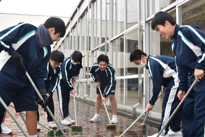 デッキブラシで中庭のタイルを磨く生徒