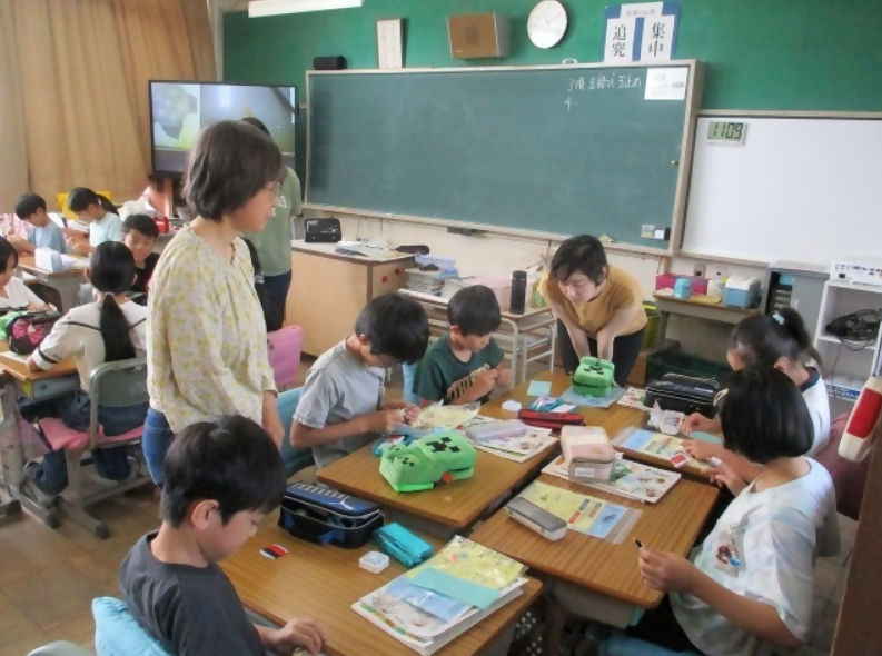 森岡小学校の5年生が、玉止め玉結びの家庭科授業でサポーターに見守られながら学習をしています。