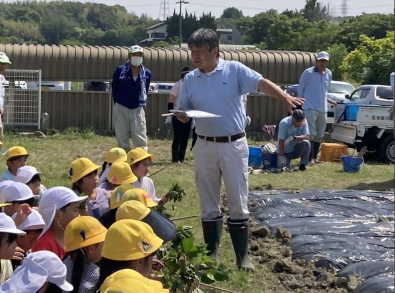 卯ノ里コミュニティの方からサツマイモの苗植え方法を聴く子どもたち
