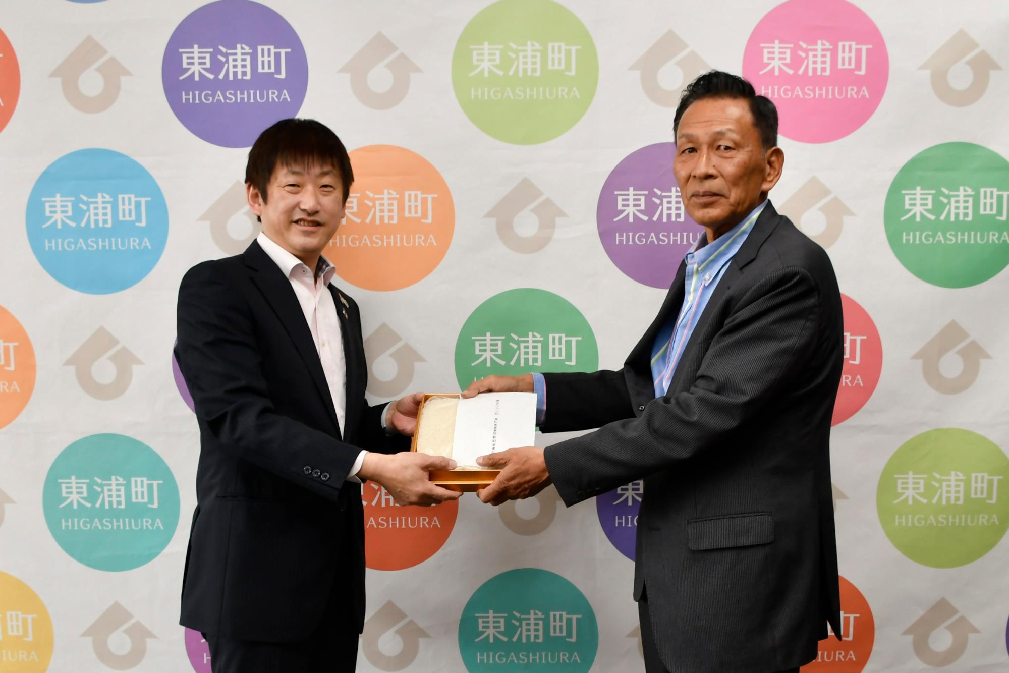 収穫米を渡す鈴木理事と受け取る日高町長