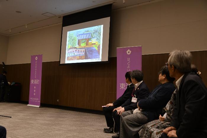 正面のスクリーンに映し出される受賞者苦品を見る参加者