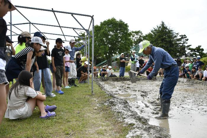 東楽会の方に畔塗りのコツを教わる児童たち