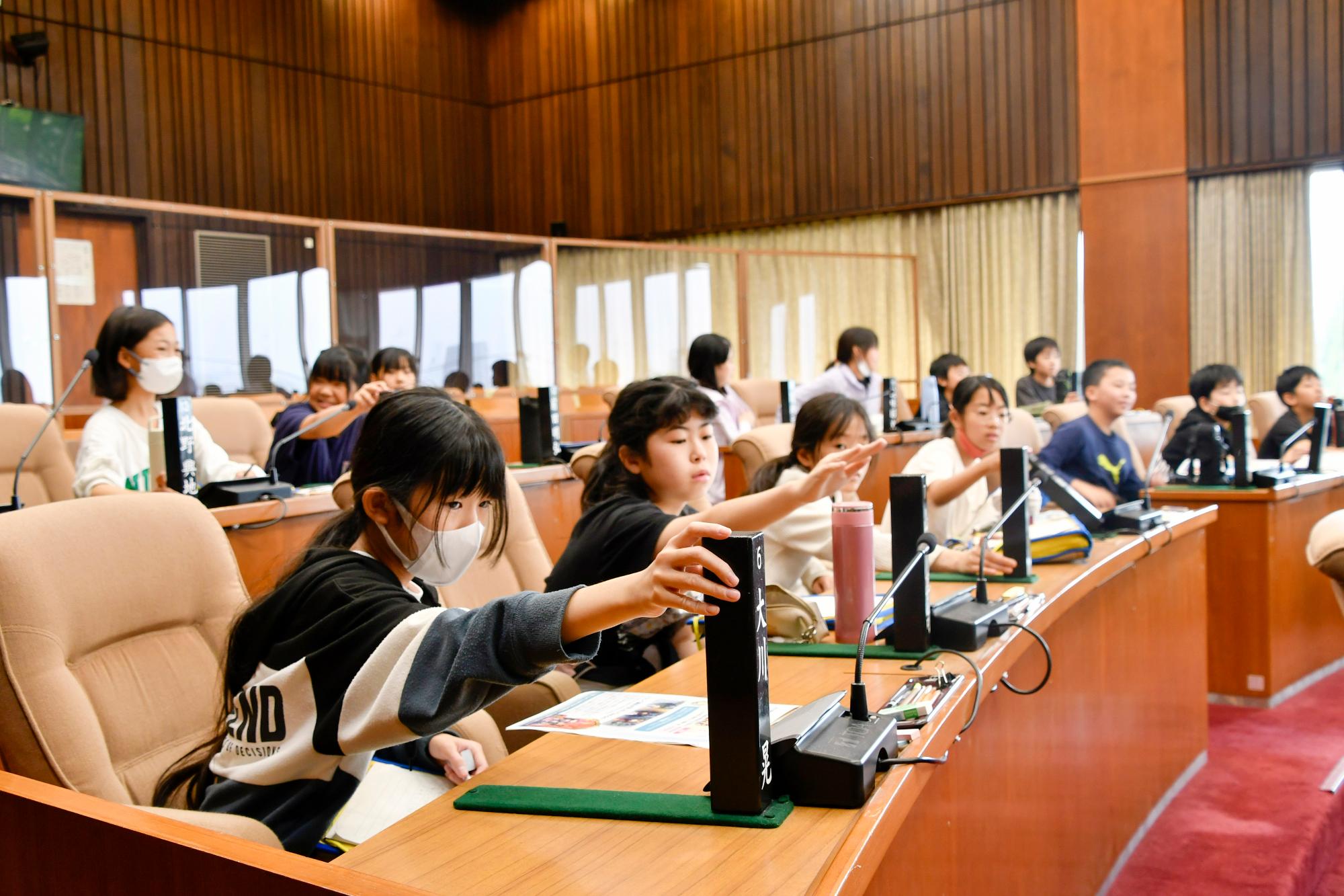 議員席に座り名札を挙げる児童たち