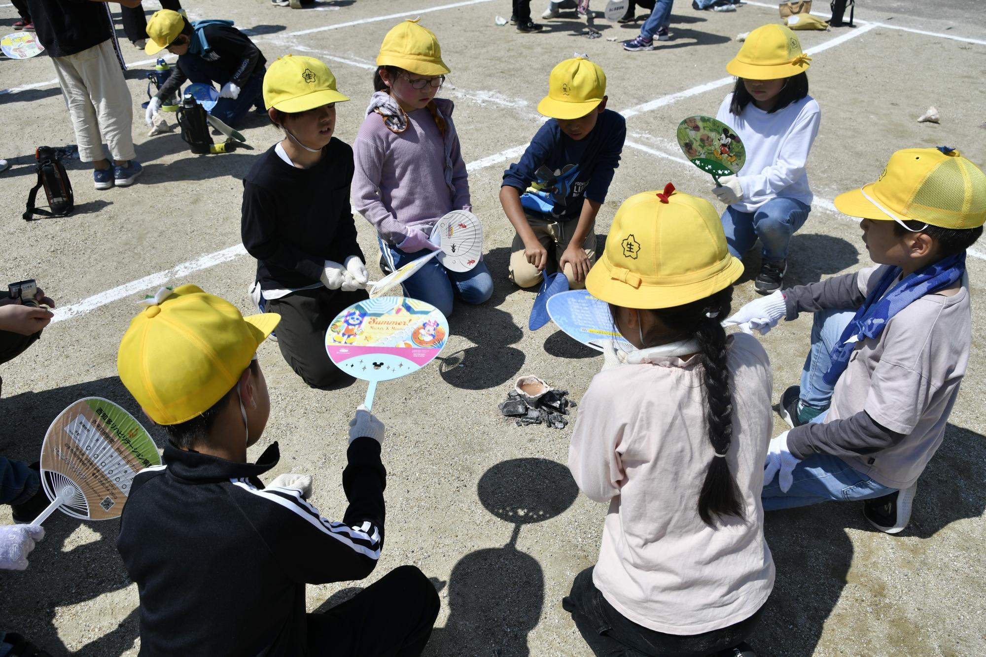 土器のまわりに置いた炭へうちわで風を送る児童